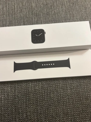 Apple Watch Series 5 – 44mm Space Gray (med låda) - Snygg Apple Watch i svart med stilren design. Klockan har en fyrkantig urtavla och svart silikonarmband. Perfekt för dig som vill ha koll på notiser, träning och hälsa direkt på handleden. Kommer i originalförpackning.