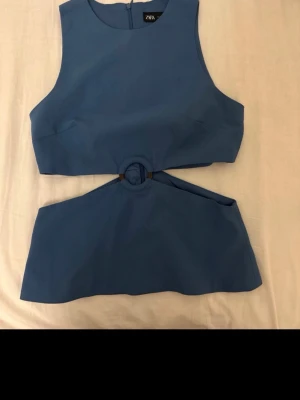 Blå croppad topp från Zara - Snygg blå topp från Zara med rund halsringning och unik cut-out detalj med ring framtill. Toppen är ärmlös och har en modern, stilren look som passar perfekt till jeans eller kjol.