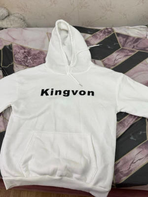 Vit Kingvon hoodie med tryck - Säljer en vit hoodie från Kingvon med svart text på bröstet och en stor grafisk bild på ryggen. Hoodien har klassisk känguruficka och dragsko i huvan. Perfekt för dig som gillar streetwear och vill sticka ut med en unik design. En gång använt det ser fortfarande nytt ut.