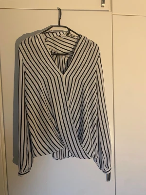 Vit och svart randig blus Gina Tricot - Blusen har omlott-design framtill, v-ringning. Materialet är tunt och perfekt till våren & sommaren. Perfekt för dig som gillar stilrena mönster och modern look.