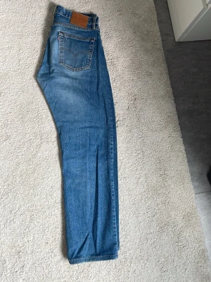 Levi's 501 blå jeans W30 L32 - Klassiska blå Levi's 501 jeans med raka ben och femficksmodell. Jeansen har en snygg vintage tvätt och är tillverkade i slitstark denim. Perfekta för dig som gillar tidlös stil och vill ha ett par ikoniska jeans i garderoben. / Uppsydda någon tum. 