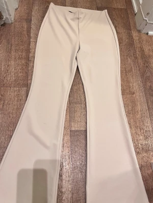Beige utsvängda leggings - Säljer ett par snygga beige leggings med utsvängda ben. De har hög midja och är sydda i ett stretchigt, mjukt material som sitter skönt på kroppen. Perfekta för dig som gillar en clean och trendig look.