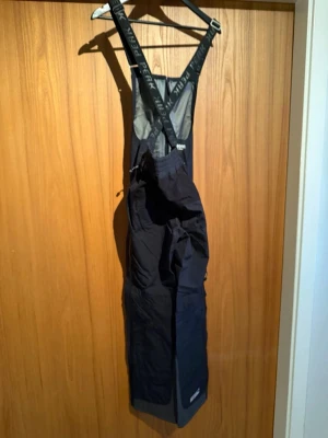 Peak Performance svarta skal byxor Gore-Tex - Peak Performance täckbyxor i svart med hängslen och förstärkta knän. Tillverkade i slitstarkt Gore-Tex Pro Shell-material, perfekt för vinterns alla äventyr. Justerbar midja, dragkedjor och detaljer med logga på benet. Sitter skönt och skyddar mot väder och vind.