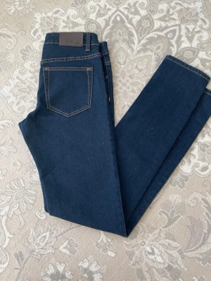 Mörkblå skinny jeans från Silvia - Snygga mörkblå skinny jeans från Silvia med klassiska femficksdetaljer och kontrastsömmar. Jeansen har hög midja och är tillverkade i stretchigt denim som ger en bekväm passform. Perfekta för dig som gillar en stilren look.