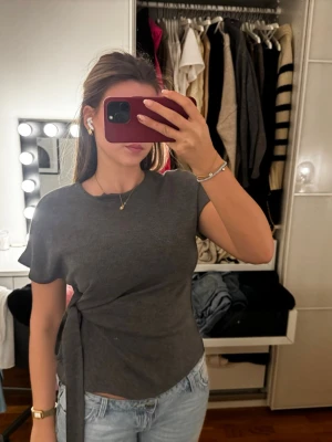 Mörkgrå topp med knyt i sidan - Säljer denna gråa topp med knut på sidan som gör att man kan justera midjestorlek! Endast använd en gång!