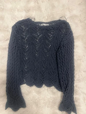 Mörkblå virkad tröja från Zara - Snygg mörkblå stickad tröja från Zara med virkat mönster och vågig kant nertill. Tröjan har lång ärm och är lätt genombruten vilket ger en luftig känsla. Perfekt att styla över ett linne eller topp för en trendig look.