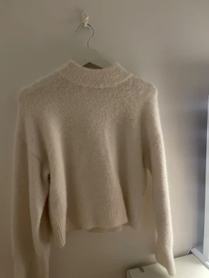 Super söt kräm vit stickad tröja!! - Mysig krämvit stickad tröja med hög hals och långa ärmar. Tröjan har en fluffig, mjuk struktur och ribbstickade muddar vid hals, ärmslut och nederkant. Perfekt för kyliga dagar och enkel att matcha till olika outfits.
