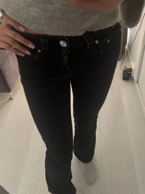 Svarta low waist jeans från Gina Tricot - Säljer ett par uttvättade svarta low waist jeans från Gina Tricot. Jeansen har smal passform, klassiska fickor och silverfärgade knappar och nitar. Jeansen är i storlek 34 men skulle säga de är tightare. Skriv till mig vid frågor eller intresse
