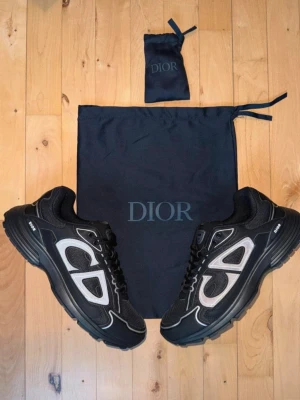 Svarta Dior sneakers med vita detaljer - PRISET SÄNKS SNABBT VID SNABBA AFFÄRER.Snygga svarta Dior sneakers med vita och grå detaljer samt tydligt CD-märke på sidan. Skorna har en chunky sula och är tillverkade i en mix av mesh och läder för en modern look. Perfekta för dig som vill ha något exklusivt och trendigt i garderoben.