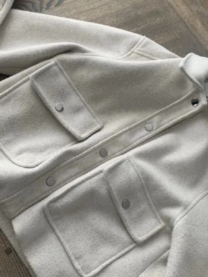 Beige/grå kappa från Zara - beige/grå kappa från Zara med två stora fickor framtill med knappar.