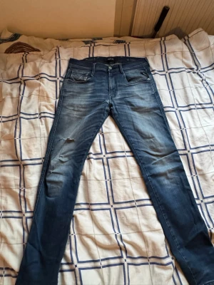 Blå skinny jeans från Replay - Säljer ett par blå skinny jeans från Replay med slitningar på vänster lår och snygg tvätt. Jeansen har fem fickor, normal midja och klassisk knappgylf. Materialet är stretchigt denim som sitter tajt och bekvämt.