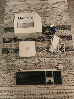 Apple Mac Mini med tangentbord och kablar - Allt fungerar som det ska. Datorn startar snabbt, går tyst Specifikationer i korthet: • Processor: Intel Core 2 Duo 1.83 GHz • RAM: 1 GB DDR2 (uppgraderingsbart till 2 GB) • Lagring: 80 GB SATA-HDD • Grafik: Intel GMA 950 • OS: Mac OS X Leopard + iLife ’08 (förinstallerat) • Anslutningar: 4× USB, FireWire, DVI, Ethernet, ljud in/ut, Wi-Fi, Bluetooth Minne: • 1 GB PC2-5300 DDR2 SDRAM (2 × 512 MB) • 667 MHz • 2 SO-DIMM-platser • Stöd för upp till 2 GB RAM Lagring: • 80 GB 2,5-tums Serial ATA-