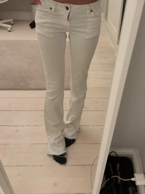 Vita bootcut jeans med låg midja - Säljer ett par vita bootcut jeans med låg midja och klassisk femficksdesign. Jeansen har en snygg, figurnära passform upptill och släpper ut lite vid bensluten. Perfekta till en trendig och avslappnad look.