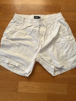 Vita shorts med snörning från 157 - Säljer ett par vita shorts från 157 i storlek M. De har elastisk midja med snörning och två sidofickor. Perfekta för varma dagar och har en avslappnad passform. Materialet känns mjukt och skönt mot huden.