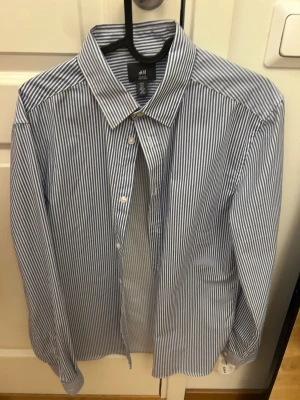 Blårandig slim fit skjorta H&M - Klassisk blårandig skjorta från H&M i slim fit-modell. Skjortan har långa ärmar, vit knappstängning och är tillverkad i bomull. Perfekt för en clean och stilren look.