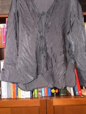 Svart crinkle-blus med knytband - Snygg svart blus i crinkle-material med två knytband framtill och v-ringning. Blusen har lång ärm, kan användas till stranden, är luftig och är köpt på ZARA i Spanien 