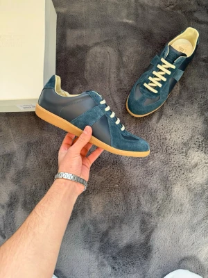 Blå sneakers med mockadetaljer - Snygga blå sneakers med ovandel i mocka och läder, beigea skosnören och klassisk gummisula. Skorna har en retroinspirerad design med låg profil och neutrala färger som passar till det mesta. Perfekta för dig som gillar stilrena och tidlösa sneakers.