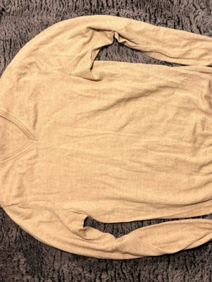 Beige stickad tröja merino - En enkel och stilren beige stickad tröja med rund halsringning och långa ärmar. Tröjan har en mjuk och tunn stickning som passar perfekt för lager på lager. Inga synliga detaljer eller mönster, bara clean och klassisk look.