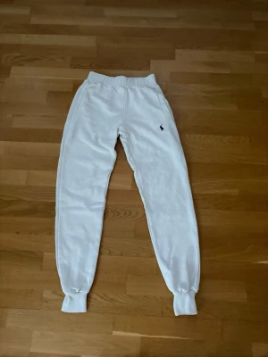 Vita mjukisbyxor från Polo Ralph Lauren - Säljer ett par vita mjukisbyxor från Polo Ralph Lauren med klassisk broderad logga på vänster sida. Byxorna har resår i midjan och vid bensluten samt sidofickor. Perfekta för en chill och avslappnad stil.