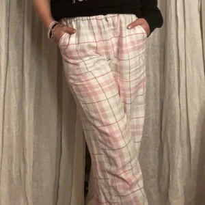 Rutiga pyjamasbyxor i rosa, grönt och vitt - Mysiga pyjamasbyxor med rutigt mönster i rosa, vitt och grön. Byxorna har resår i midjan och raka ben, perfekta för chillkvällar hemma. Tillverkade i mjukt tyg som känns skönt mot huden.