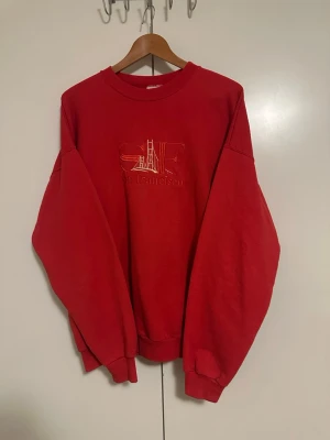 Röd sweatshirt med San Francisco-brodyr - Cool röd sweatshirt med broderad text 'San Francisco' och motiv av Golden Gate-bron på bröstet. Oversized passform med ribbade muddar vid ärmslut och nederkant. Perfekt för dig som gillar streetwear och vill ha en unik detalj i garderoben.