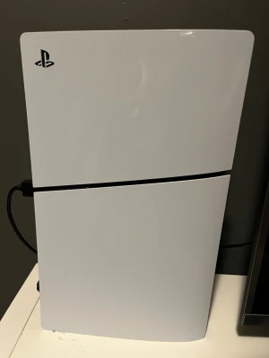 PlayStation 5 spelkonsol vit - PlayStation 5 från Sony i snygg vit och svart design. Konsolen har en futuristisk form med rundade kanter och matta paneler i plast. Perfekt för gaming med kraftfull prestanda och stöd för de senaste spelen. Det följs även med NHL 25 och FC25