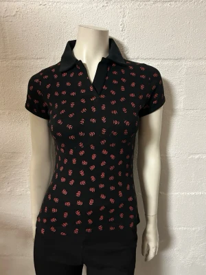 Topp från Poizen i storlek L/XL. - Helt ny topp med krage. Storlek L/XL. Små döskallar. Stretchig bomullstrikå.