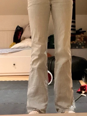 Ljusblå bootcut jeans med dubbla knappar - Säljer ett par ljusblå bootcut jeans med dubbla metallknappar i midjan och klassiska bälteshällor. Jeansen har en utsvängd passform nedtill och är tillverkade i denim. Perfekta för dig som gillar retrovibbar och vill ha ett par snygga jeans med unik detalj i midjan.