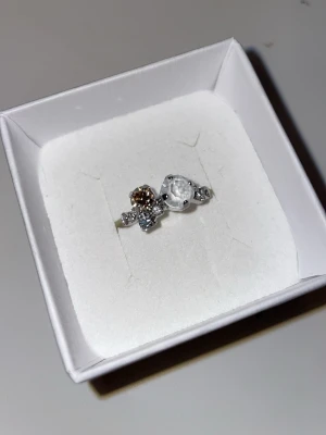 Caroline Svedbom silverring med stenar - Snygg silverfärgad ring från Caroline Svedbom med flera gnistrande stenar i olika storlekar och färger, bland annat klar och champagne. Ringen har en modern och unik design som verkligen sticker ut.