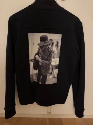 Limitato Sweatshirt  - Snygg svart tröja med silverfärgade dragkedjor och två fickor framtill. På ryggen finns ett stort svartvitt fototryck med motiv av Jimi Hendrix. Tröjan har ribbade muddar och klassisk bomberkrage.