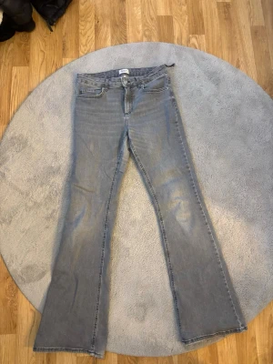 Ljusblå bootcut jeans - Säljer ett par ljusgråa bootcut jeans med klassisk femficksdesign och dragkedja. Jeansen har en lätt tvättad look och är tillverkade i denim. Perfekta för dig som gillar en avslappnad men ändå trendig stil. Lite trasiga vid sidan och sönder trampade ner till, men jätte sköna och fina!
