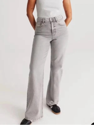 Gråa bootcut jeans - Säljer ett par ljusgrå bootcut jeans med hög midja och klassisk femficksdesign. Jeansen har vida ben och är tillverkade i ett mjukt denimtyg som ger en avslappnad men snygg look. Perfekta för dig som gillar retrovibbar och vill ha ett par jeans som sticker ut.