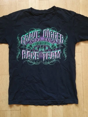 Vintage 00s Gravedigger (Monster Jam) T-Shirt | S / Small | Retro Y2K - Vintage T-Shirt med Gravedigger - Monster Jam tryck på framsidan och baksidan.  Small (Mått finns på bilderna!)  Se bilder.  "Monster Jam är en liveshow inom motorsport som drivs av Feld Entertainment. Serien startade 1992 och är sanktionerad under United States Hot Rod Association"