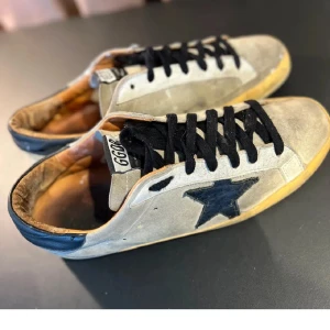 Golden Goose - Snygga beige sneakers från Golden Goose med svart stjärndetalj på sidan, svarta skosnören och kontrasterande svart häl. Ovandel i mocka och klassisk platt sula i gummi. Perfekta för en avslappnad streetstyle-look. De är en del heeldrag men de får man för priset.  Priset är inte huggit I sten 
