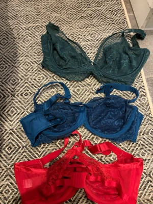 3-pack spetsbhar i grönt, blått och rött - Säljer tre snygga bhar i spets, en mörkgrön, en mörkblå och en röd. Alla har dekorativa banddetaljer och genombruten spets framtill. Den röda har extra band över bysten för en trendig look. Perfekt för dig som gillar färg och detaljer.