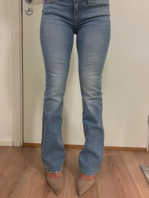 Ljusblå bootcut jeans från Levi's - Säljer ett par ljusblå bootcut jeans från Levi's med klassisk femficksmodell och snygg slitning framtill. Jeansen har normal midja, Levi's ikoniska läderpatch bak och röd logotagg på bakfickan. Perfekta till sneakers eller boots! Storlek 27