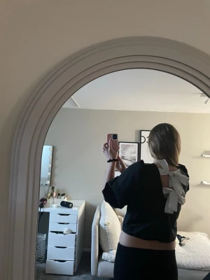 Svart topp med rosett - Svart topp med puffärmar och två vita rosetter i ryggen. Toppen har fyrkantig ringning och öppen rygg.🥰