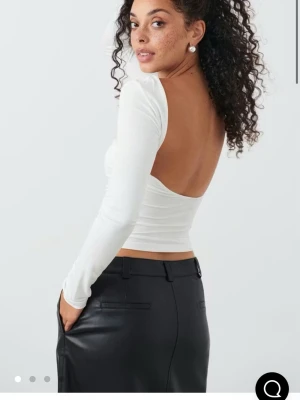 Vit långärmad topp med öppen rygg - Trendig vit långärmad topp med tight passform och öppen rygg. Toppen är croppad och har en enkel, stilren design som passar perfekt till både kjol och byxor. Bara använd 1 gång