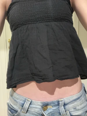 Svart bandeau topp från Gina Tricot - Säljer en svart bandeau topp från Gina Tricot. Toppen är axelbandslös med smock upptill och har en luftig, lätt utställd passform. Perfekt till sommaren och enkel att matcha med jeans eller kjol.