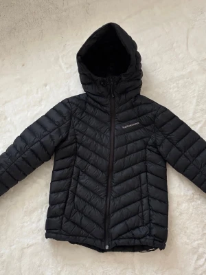 Svart pufferjacka från Peak Performance - Säljer en svart pufferjacka från Peak Performance med huva och dragkedja framtill. Jackan har ett snyggt mönster av diagonala sömmar och två sidofickor med dragkedja. Perfekt för kalla vinterdagar och riktigt skön att bära.