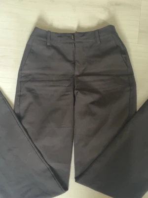 Svarta kostymbyxor från BikBok - Snygga Svarta kostymbyxor från BikBok i rak modell med hög midja och bälteshällor. Byxorna har sidfickor och stängs med dragkedja och knapp. Perfekta för en clean och stilren look.