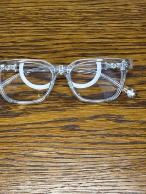 Chrome hearts  - Säljer ett par unika transparenta solglasögon med fyrkantig form och blommiga detaljer på bågarna. Ramen är helt genomskinlig och har snygga blommönster vid gångjärnen och på skalmarna. Perfekt accessoar för dig som vill sticka ut.