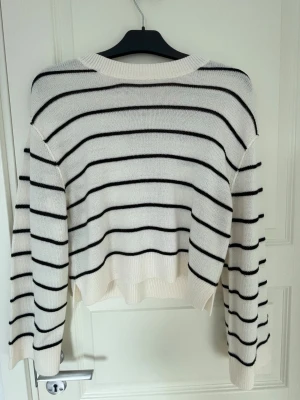 Knitted stripped sweater - Säljer en vit stickad tröja med svarta horisontella ränder. Tröjan har en avslappnad passform, rund halsringning och långa ärmar. Ribbstickade muddar vid ärmslut och nederkant. Perfekt för dig som gillar klassisk och enkel stil.
