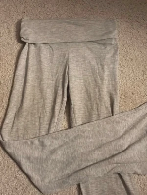 Grå mjukisbyxor från H&M - Säljer ett par ljusgrå mjukisbyxor från H&M med bred, vikbar midja och raka ben. Tillverkade i mjukt och stretchigt material som är skönt att ha på sig. Perfekta för chill dagar eller när du vill vara bekväm.