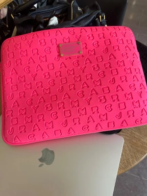 Rosa datorväska Marc by Marc Jacobs - Säljer en snygg datorväska i starkt rosa från Marc by Marc Jacobs. Väskan har präglade bokstäver över hela ytan och en metallbricka framtill. Tillverkad i vadderat material som skyddar din laptop och ger en cool look.