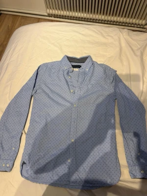 Ljusblå skjorta från Jack & Jones - Snygg ljusblå skjorta från Jack & Jones Premium med små mörka prickar. Skjortan har klassisk krage, knappar framtill och långa ärmar. Tillverkad i mjuk bomull som känns skön mot huden. Perfekt för dig som gillar stilrena detaljer.