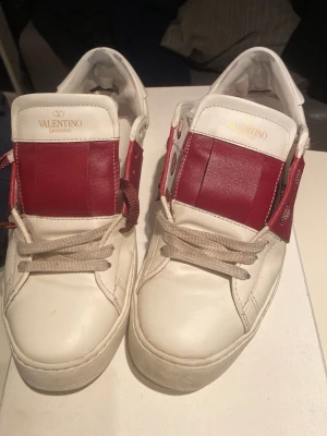 Valentino Garavani open vita och röda sneakers - Skriv privat för mer bilder,de är lite sunkiga innuti men utanpå så ser de nästan nya ut förutom på bild 5 där man kan se en pytteliten gul fläck, på bild 4 syns även att sulan är nedgången, men jag tycker själv att det inte påverkade något, skosnörena är lite smutsiga, annars är de i bra skick utåt sätt.