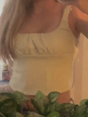 Gul croppad linnetopp - Söt ljusgul croppad linnetopp med breda axelband och lätt rynkade detaljer vid bysten. Toppen har en enkel och fräsch design som passar perfekt till jeans eller kjol under varma dagar.