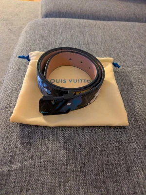 blommigt bälte - Snyggt bälte från  med svart bas och färgglatt blommigt mönster. Bältet har en svart spänne och insidan är i ljust brunt skinn. Perfekt för att lyfta vilken outfit som helst.