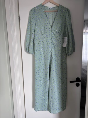 Grön blommig långklänning . Bubbleroom - Ljusgrön långklänning från bubbleroom v-ringning, trekvartsärmar med resår och en lätt figurnära passform. Perfekt för vår och sommar med sitt tunna, luftiga material.